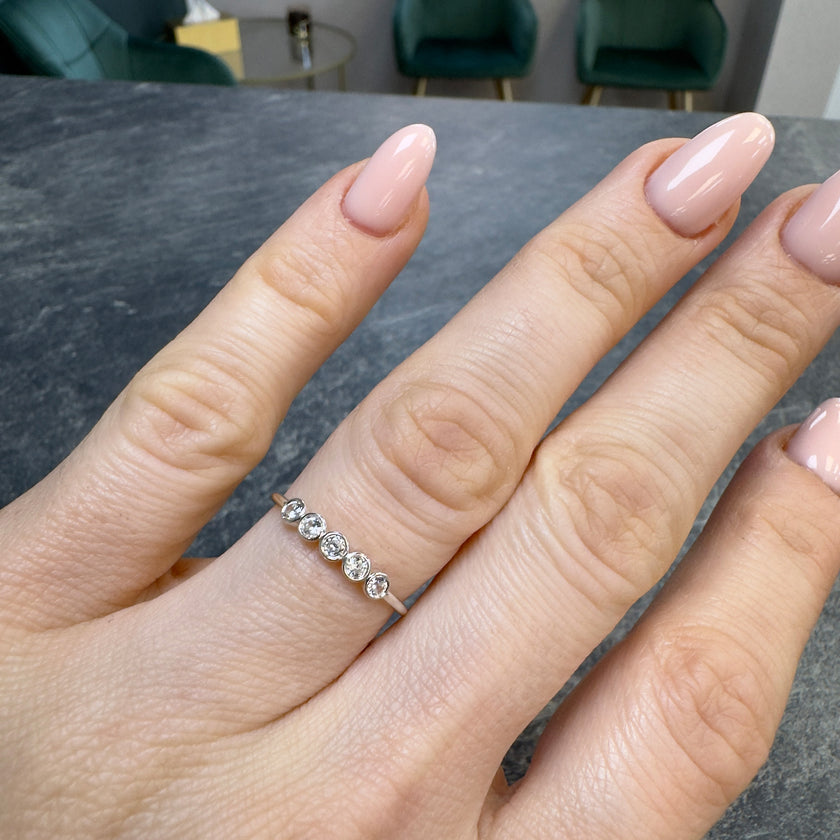 A real-life lifestyle photograph of the Luna 14K white gold ring worn on a woman's hand, showcasing the five brilliant-cut lab-grown diamonds in a protective bezel setting and its sleek, low-profile design.